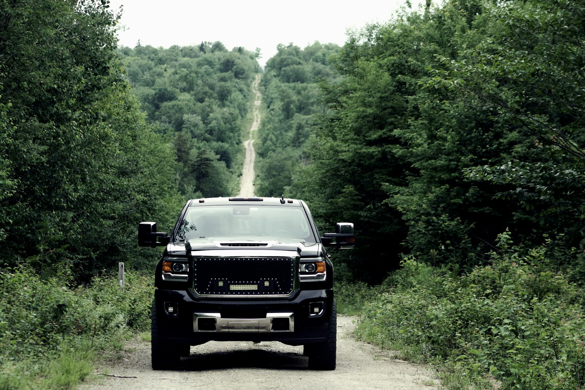 a truck driving down a dirt road through a forest