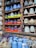 An assortment of colorful ceramic vases and pots are displayed in a wooden shelf. The ceramics come in bright colors such as blue, orange, green, and brown, with various patterns and textures. A small chalkboard sign reads 'Made in Vietnam' with a price range. Additionally, several ceramic animal figures resembling chickens are placed on a lower shelf amidst more blue vases.
