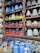 An assortment of colorful ceramic vases and pots are displayed in a wooden shelf. The ceramics come in bright colors such as blue, orange, green, and brown, with various patterns and textures. A small chalkboard sign reads 'Made in Vietnam' with a price range. Additionally, several ceramic animal figures resembling chickens are placed on a lower shelf amidst more blue vases.