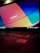 A laptop keyboard is visible with an open screen displaying a blurred multicolored desktop background. The colors are vivid, with prominent shades of blue, orange, and red. An Intel sticker is in focus on the laptop's palm rest area.