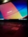 A laptop keyboard is visible with an open screen displaying a blurred multicolored desktop background. The colors are vivid, with prominent shades of blue, orange, and red. An Intel sticker is in focus on the laptop's palm rest area.