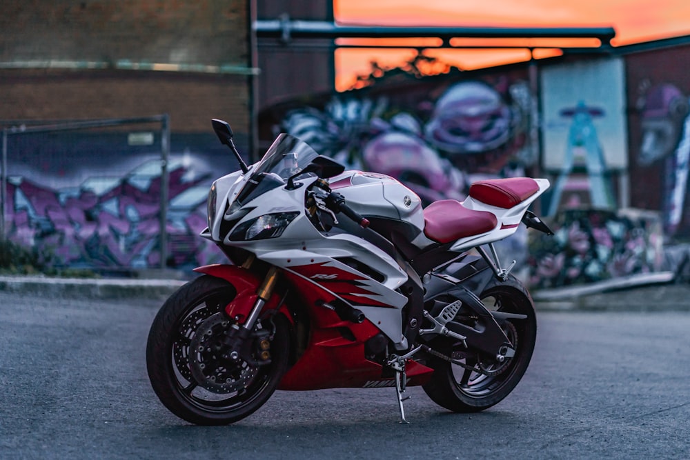 a red and white motorcycle parked in front of a graffiti covered wall