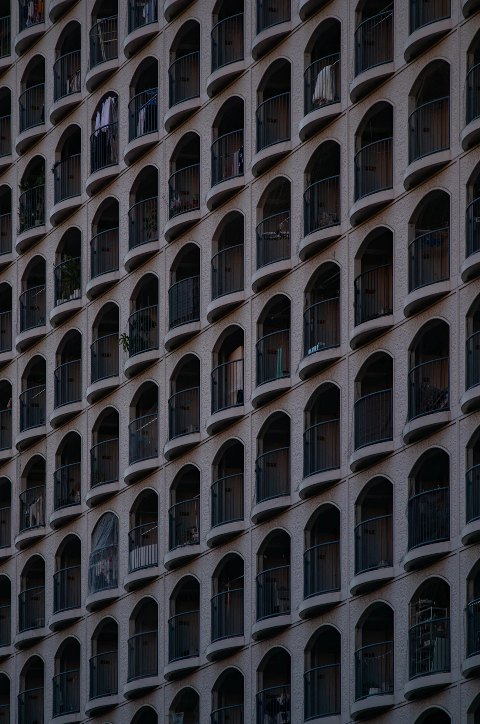 Close-up view of apartment building with numerous arched windows and unique balconies constructed from gray