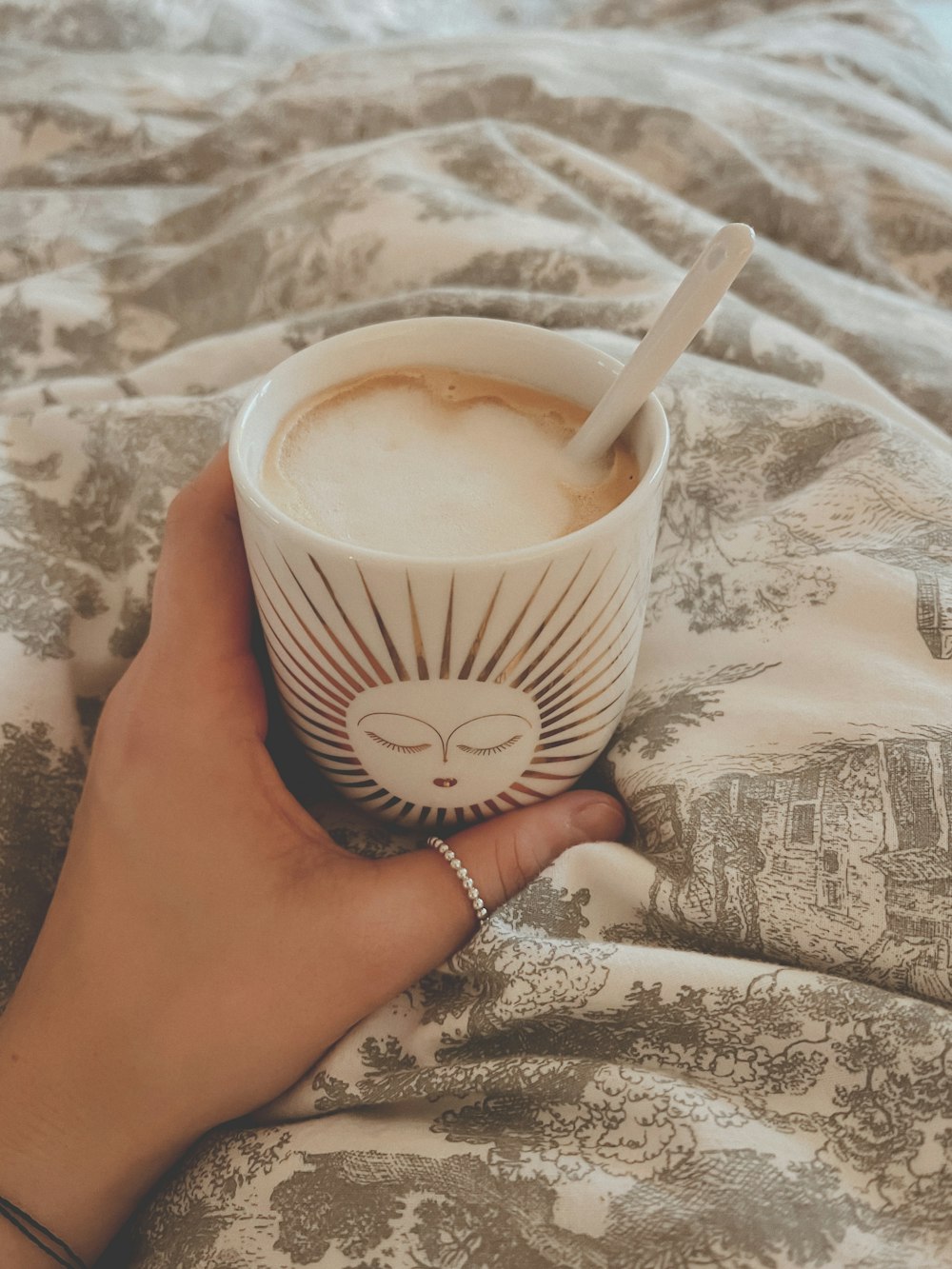 a person holding a cup of coffee on top of a bed