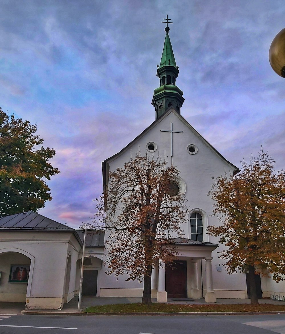 a white church with a green steeple on a cloudy day