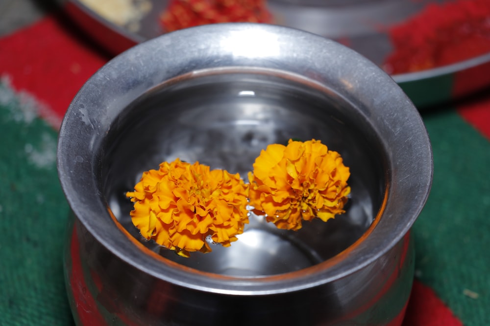 two yellow flowers are in a metal bowl