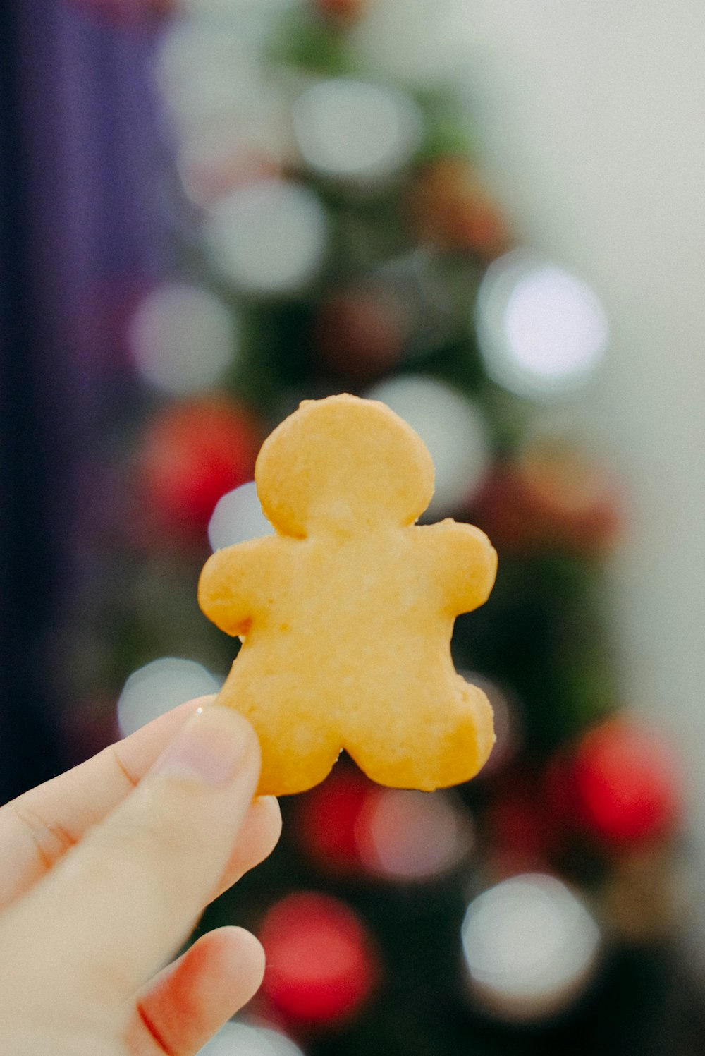 a person holding a small cookie in front of a christmas tree