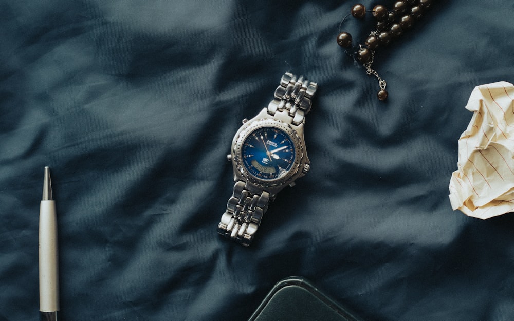 a watch, rosary, and pen on a blue cloth