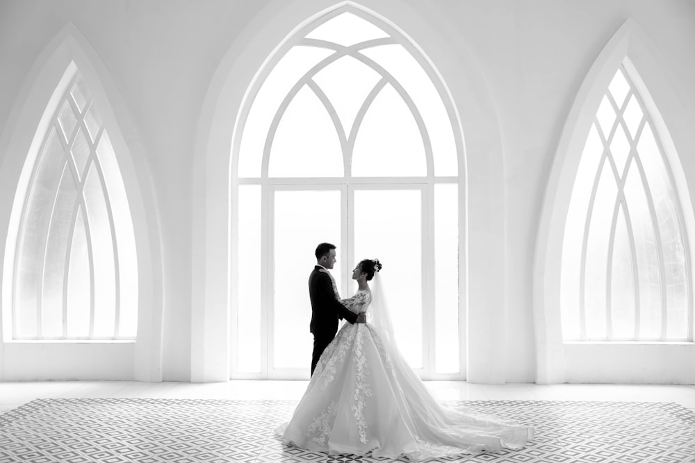 a bride and groom standing in front of a large window