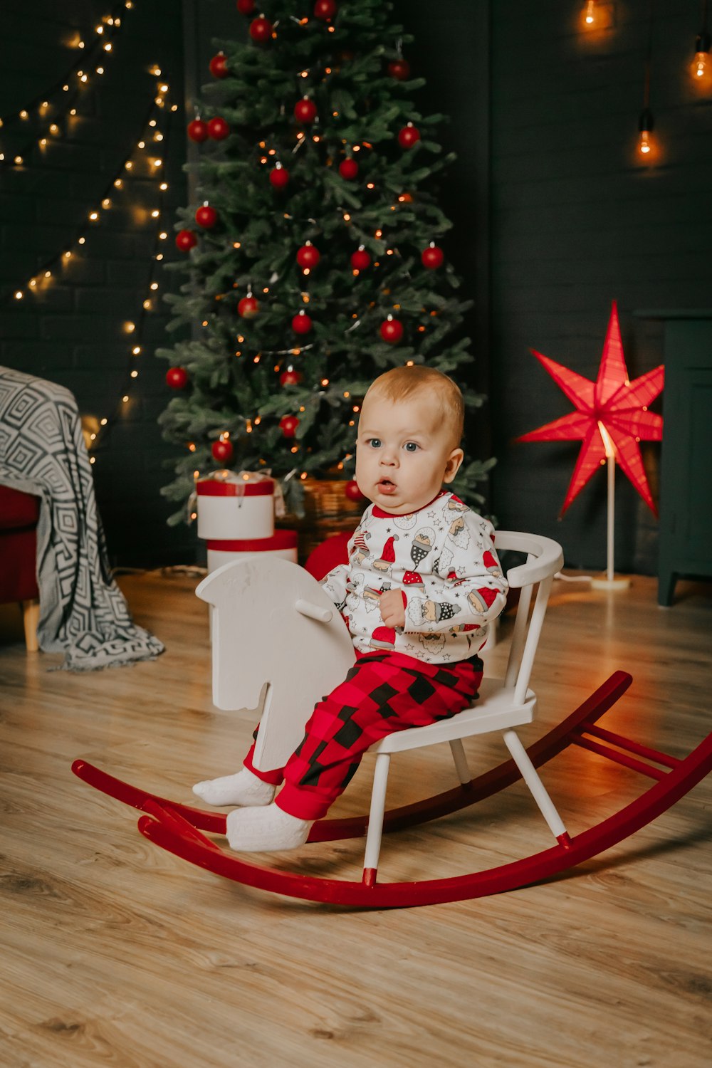 a baby sitting in a rocking chair next to a christmas tree