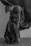 A person is wrapped in a large, flowing fabric that drapes around their body. The artistic pose highlights the figure's physique and grace. The setting is minimalist, with a wooden floor and a plain background, creating a serene and introspective atmosphere.