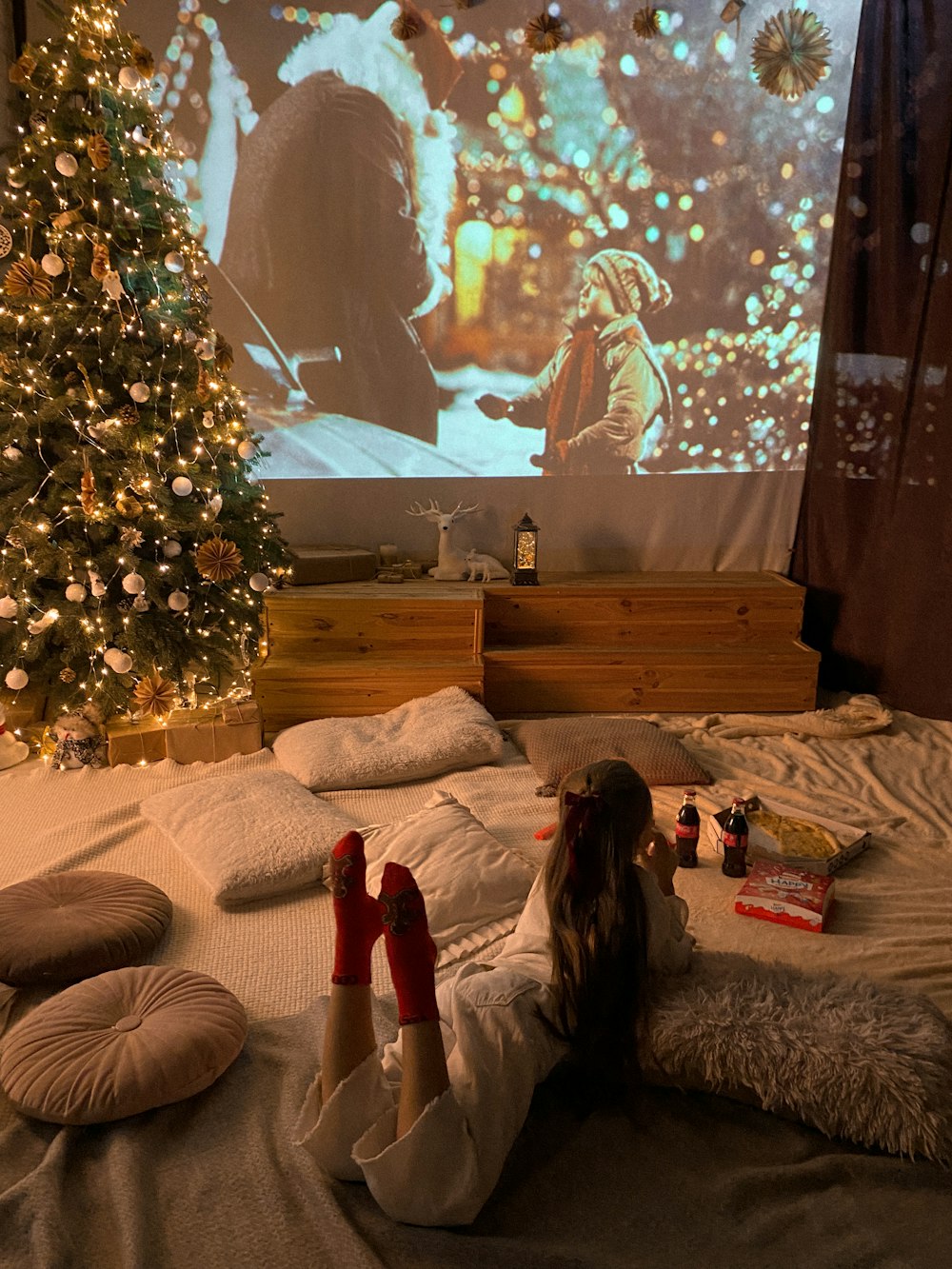 uma menina deitada em uma cama na frente de uma árvore de Natal