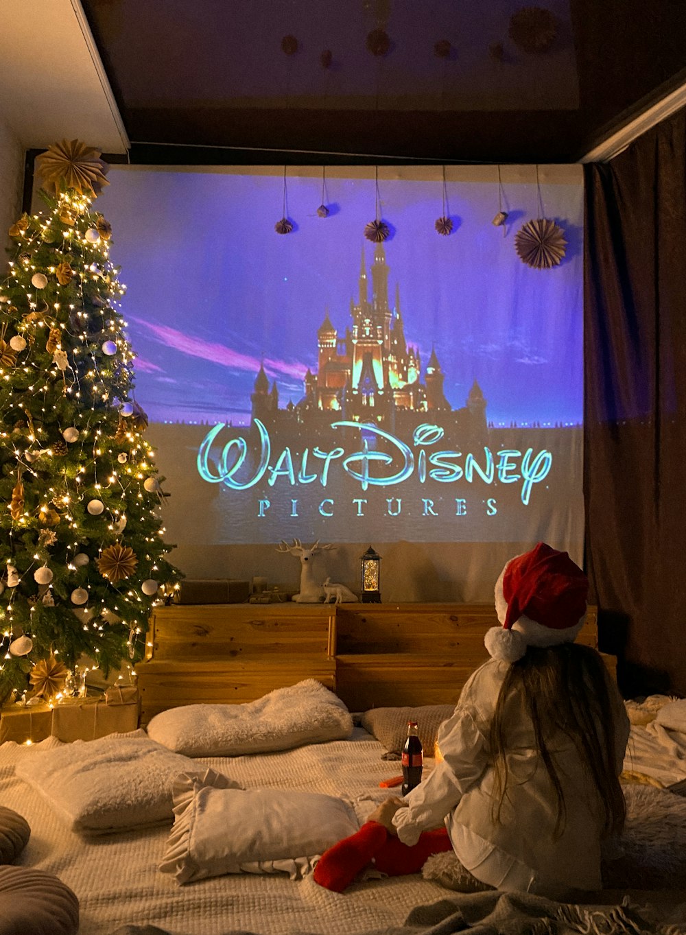 a little girl sitting on a bed in front of a christmas tree