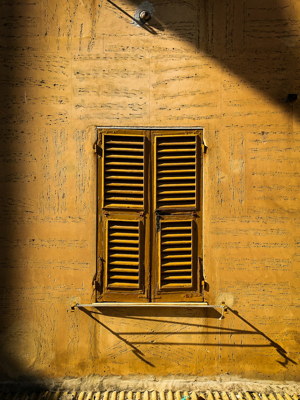 a yellow building with a wooden window and shutters