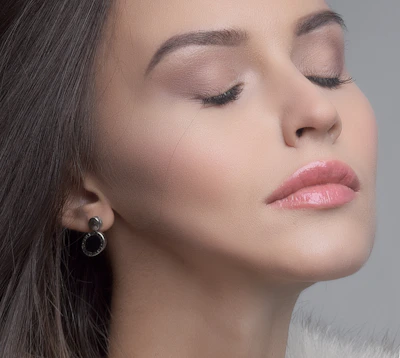 Elegant close-up of a refined woman receiving a gentle facial consultation in a serene, softly lit clinic room with pink accents.