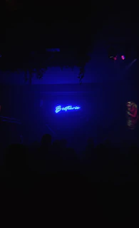 A dimly lit 1980s Johannesburg nightclub entrance glowing with neon lights and shadowy figures.