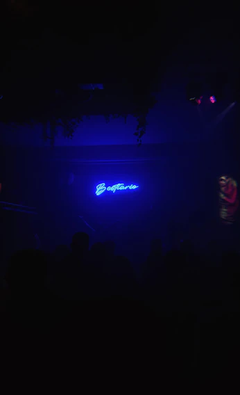 A dimly lit 1980s Johannesburg nightclub entrance glowing with neon lights and shadowy figures.