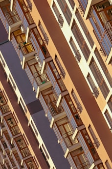 A high-rise building featuring a repetitive pattern of windows and balconies with wooden accents. The structure has a modern architectural design with a warm color palette and appears to be taken from an angled perspective.