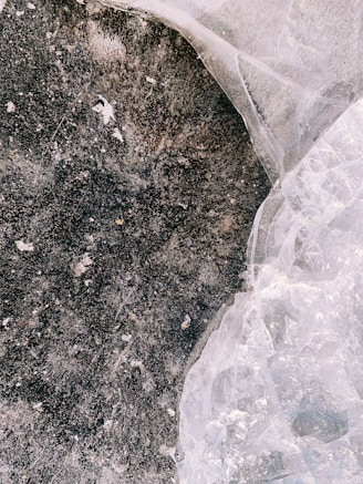 A close-up textured surface features a dark, earthy area with circular patterns and a contrasting, translucent crystalline or icy section. The surface appears weathered and organic.