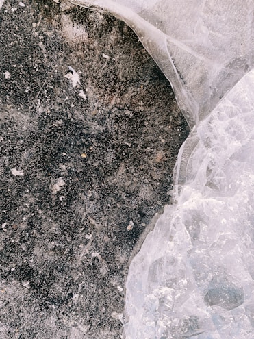 A close-up textured surface features a dark, earthy area with circular patterns and a contrasting, translucent crystalline or icy section. The surface appears weathered and organic.