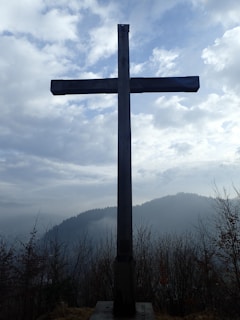 A quiet, humble cross standing in a simple rural landscape at dawn.