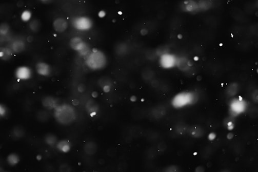 Floating white particles against a dark background, creating a sense of movement and depth.