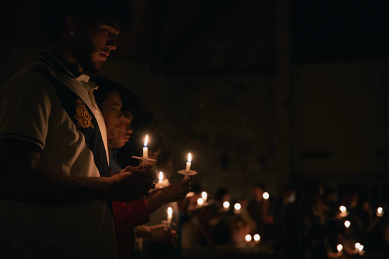 A warm, softly lit scene of young people sharing a moment of prayer and laughter, surrounded by delicate golden light accents.