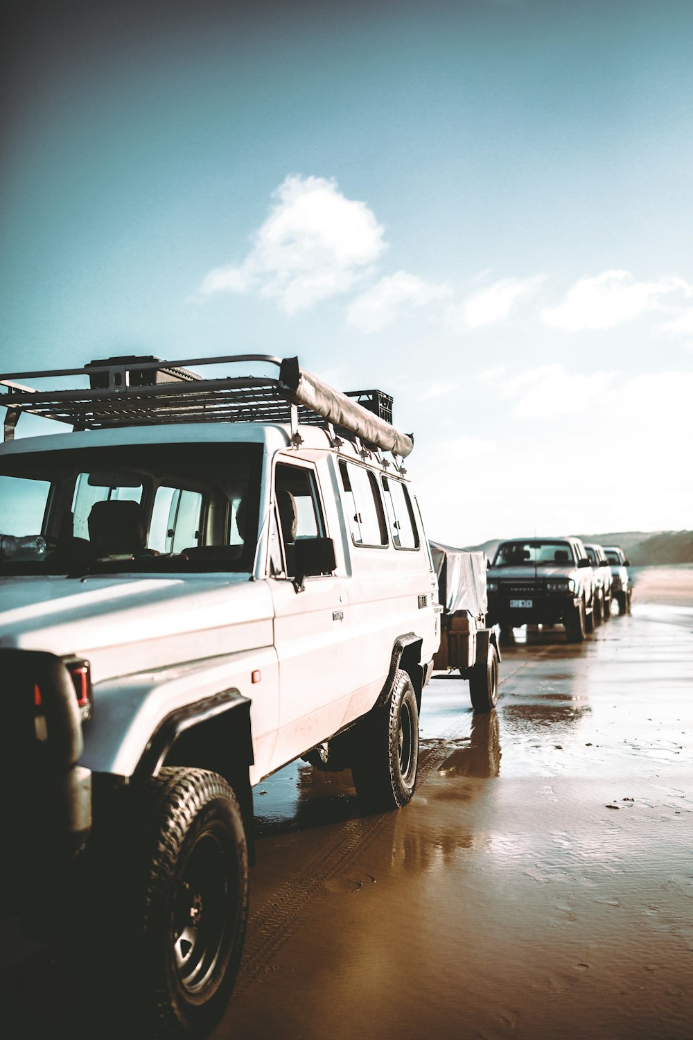 um grupo de quatro veículos estacionados em uma praia molhada