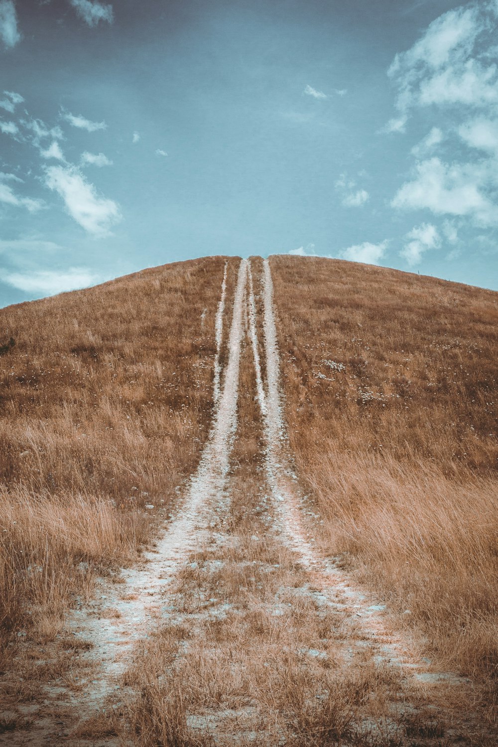 a dirt road going up a hill with a sky background