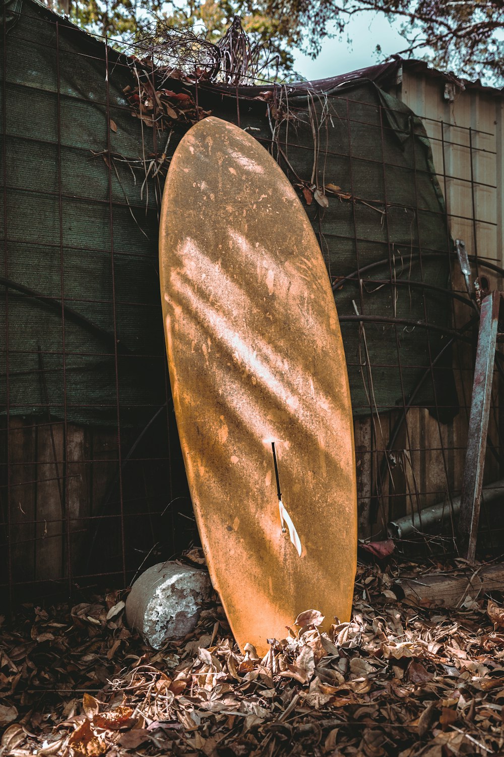 a rusted surfboard leaning against a fence
