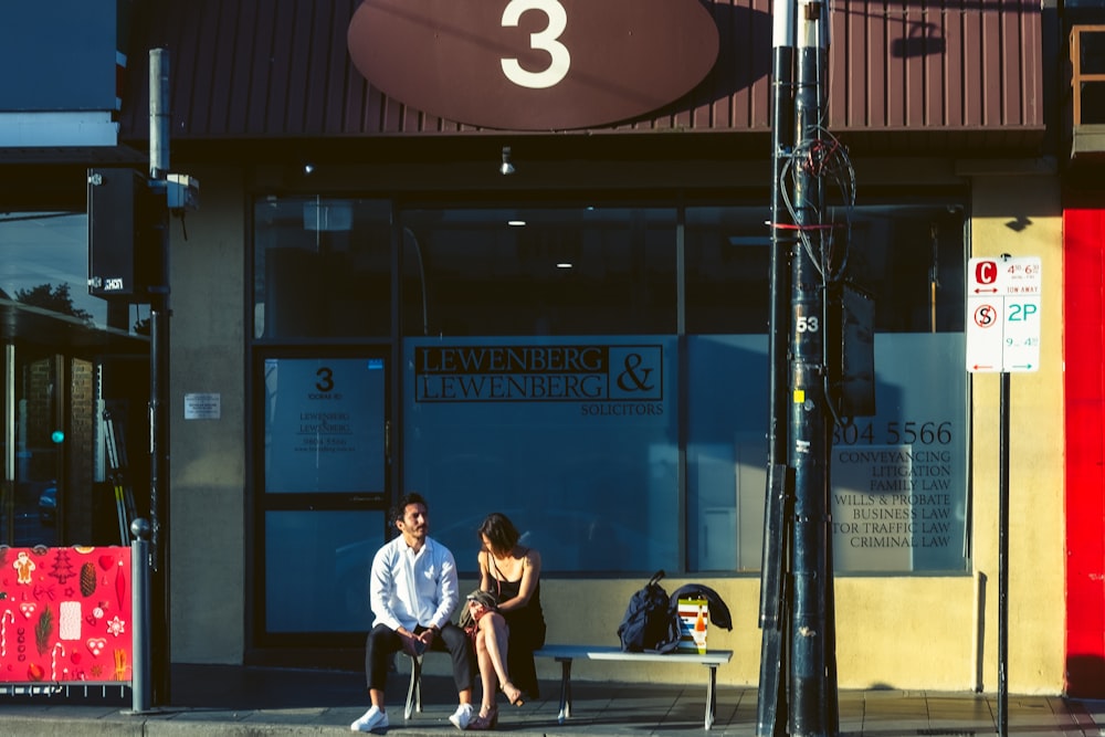 a man and woman sitting on a bench in front of a building