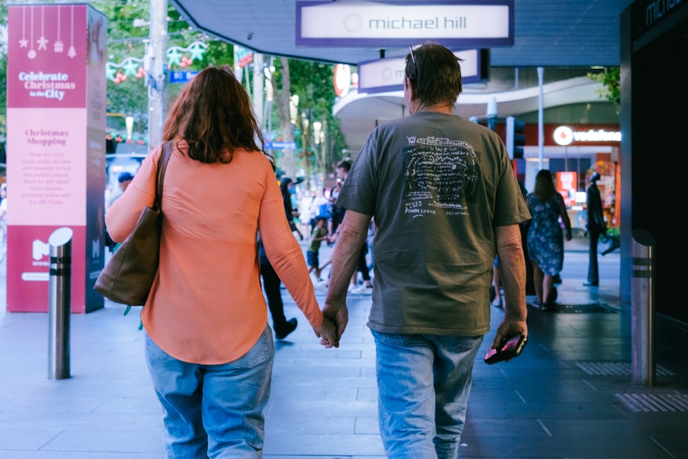 a man and woman walking down a sidewalk holding hands