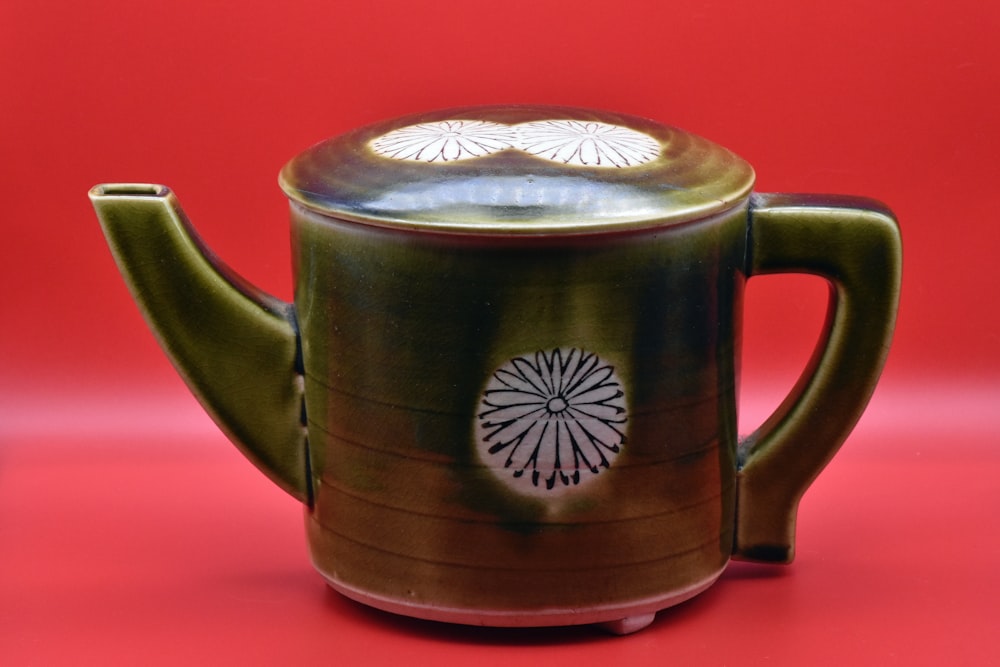 a green teapot with a white flower on it