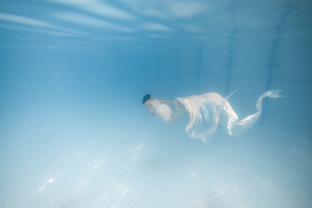 a woman in a white dress swimming under water
