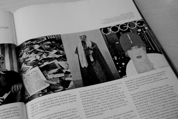 A black and white image of an open magazine displaying multiple pages. On the left page, there is a collage of numerous photographs and a headline that reads 'The Birth of Vogue'. The right page features a vintage Vogue cover with a stylishly drawn woman wearing a hat, set against a patterned background.