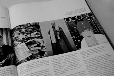 A black and white image of an open magazine displaying multiple pages. On the left page, there is a collage of numerous photographs and a headline that reads 'The Birth of Vogue'. The right page features a vintage Vogue cover with a stylishly drawn woman wearing a hat, set against a patterned background.