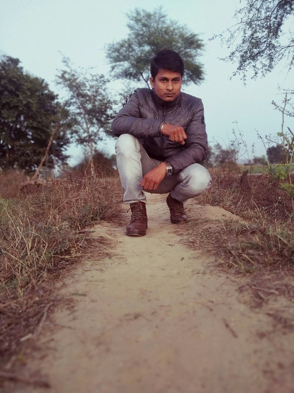 a man squatting down on a dirt path