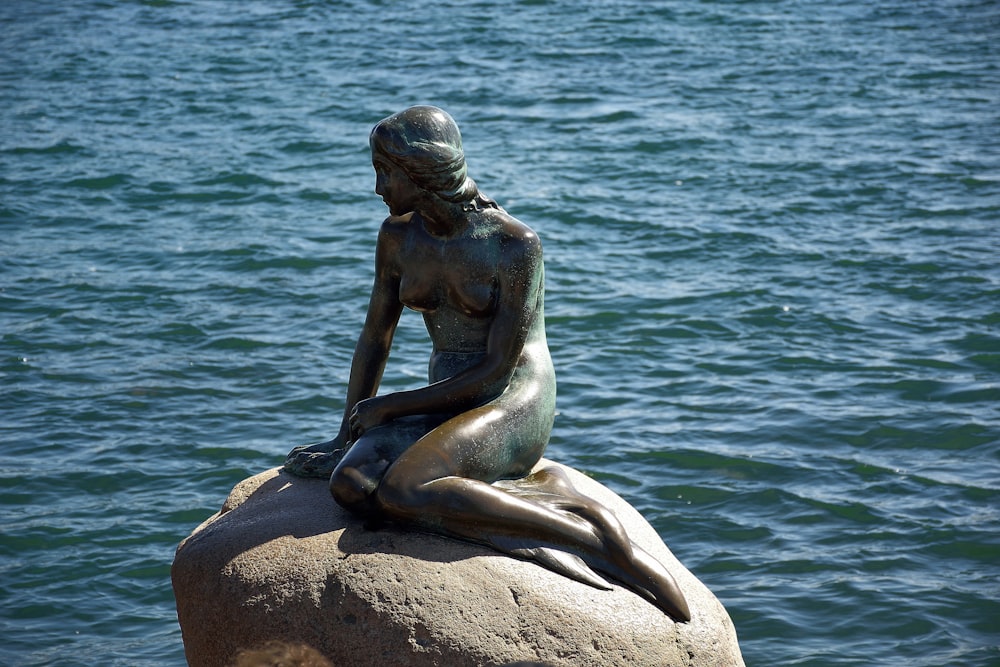 uma estátua de uma sereia sentada em uma rocha