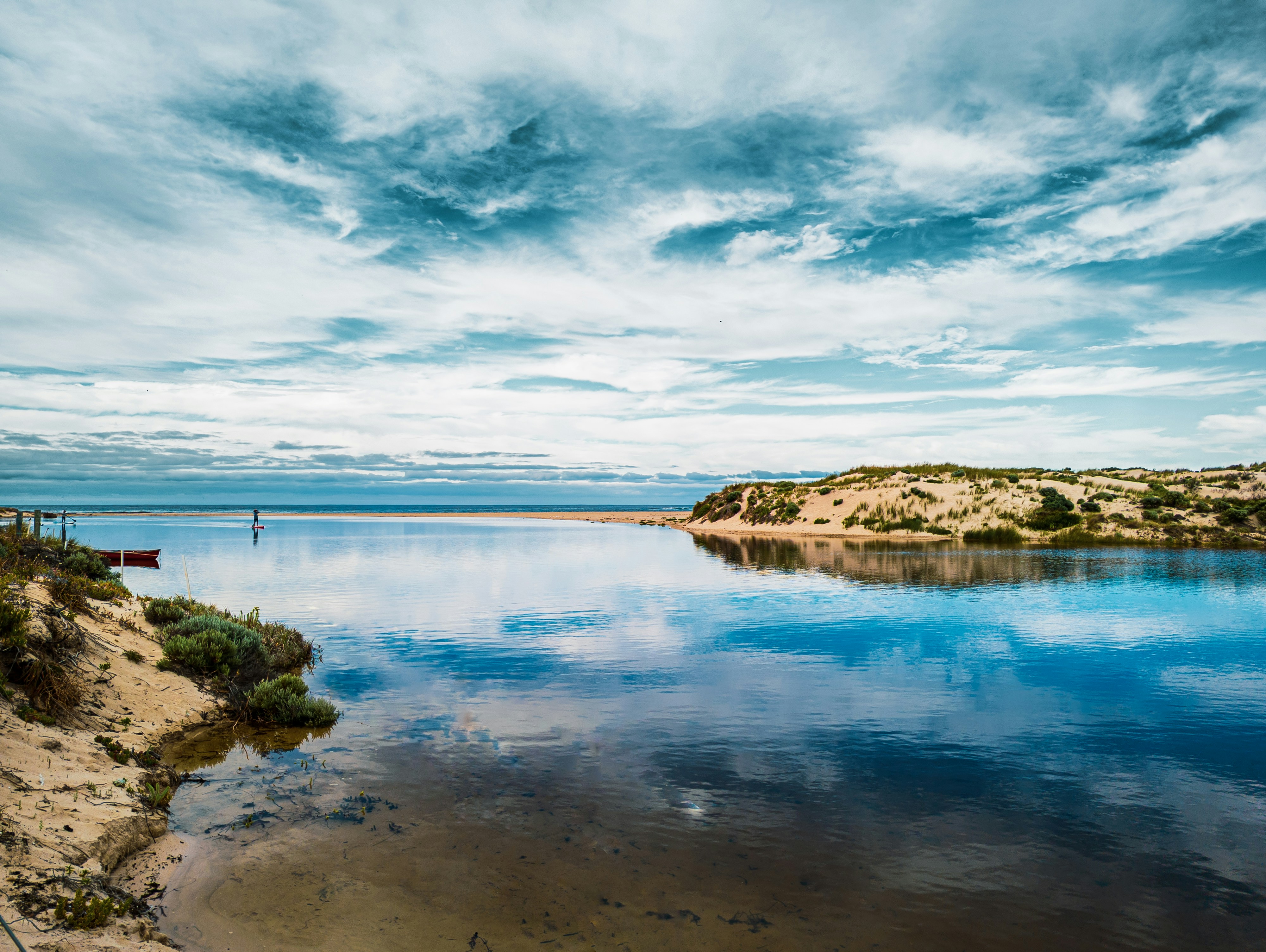 a body of water surrounded by a sandy shore, Paddle boarder paddling through the Margaret River Mouth