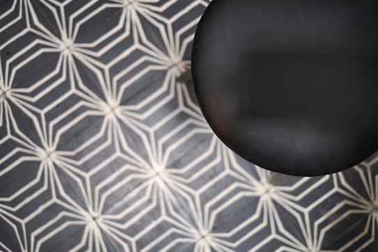 A black circular object is partially visible against a geometric-patterned background. The pattern consists of interconnected white lines forming hexagonal shapes on a dark background.