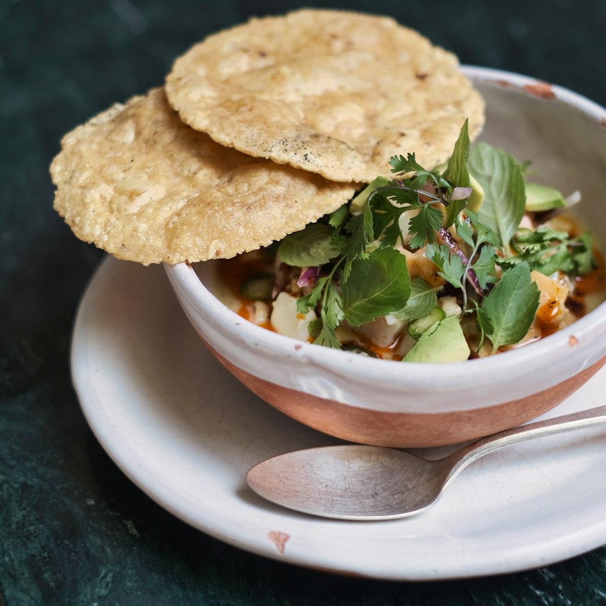 Small bowls of tortilla soup toppings — avocado, cotija cheese, cilantro, lime wedges and crema arranged for serving