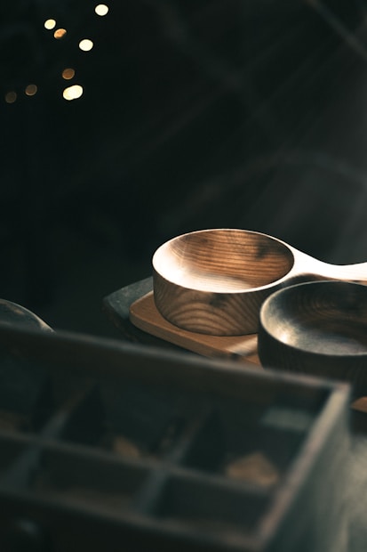 Two wooden bowls are placed on a wooden table, illuminated by soft, natural light. The setting includes a dark background with some bokeh lights, creating a warm and rustic atmosphere.