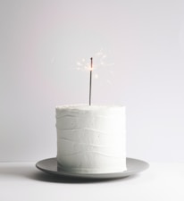 Minimalist styled cake setup featuring a smooth caramel-toned cake on a matte white surface.