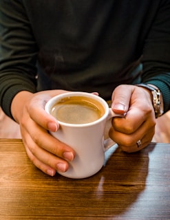 Hands holding a steaming cup of black coffee over a rustic wooden table