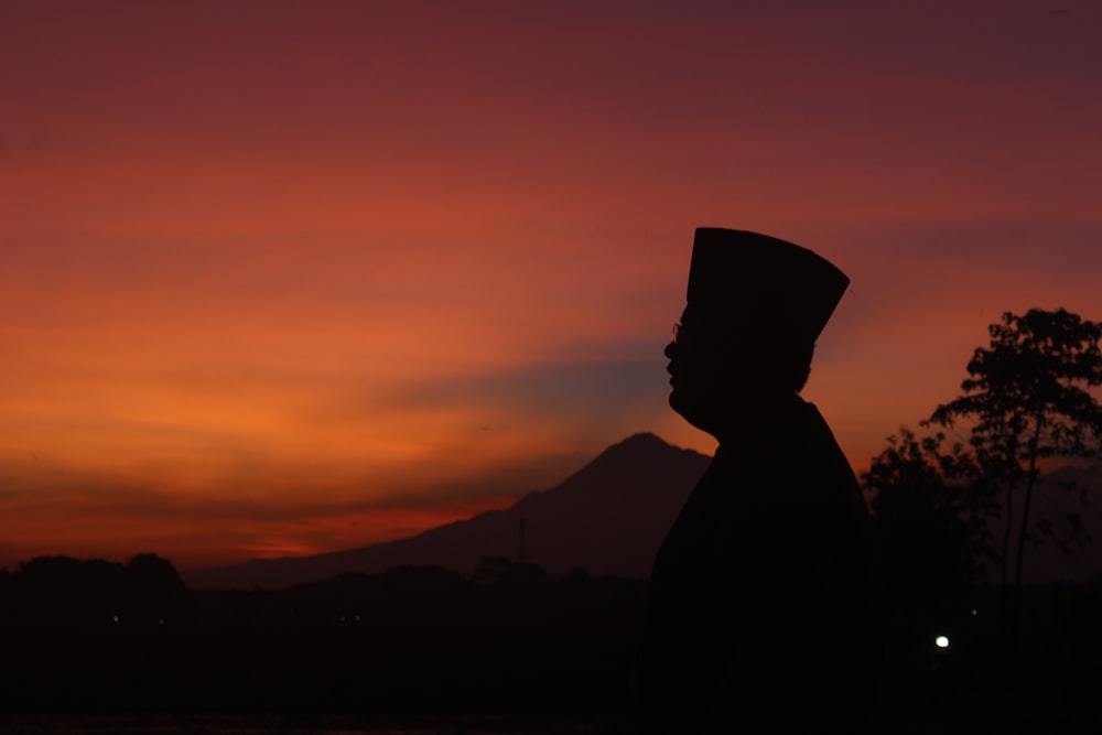 a silhouette of a man wearing a hat at sunset