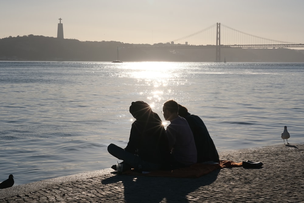 a couple of people sitting on top of a beach next to a body of water