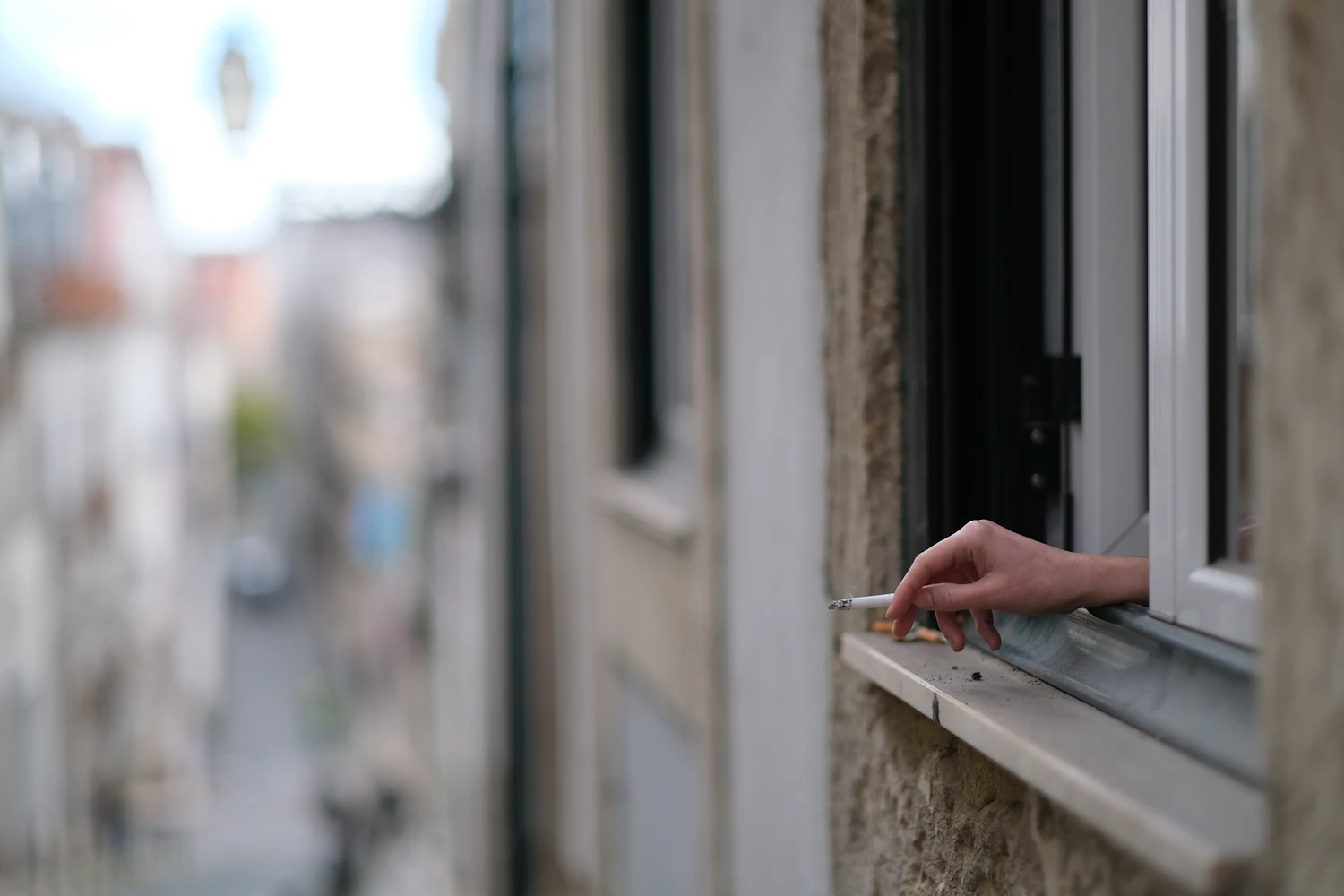 Hand hält eine Zigarette an einem geöffneten Fenster