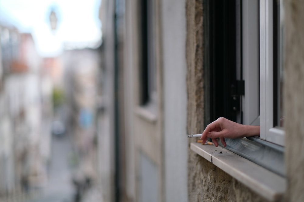 a person's hand on a window sill holding a cigarette