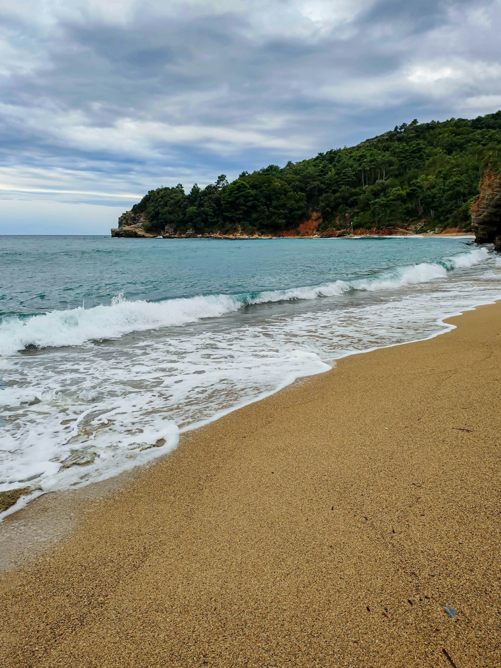 a sandy beach next to the ocean under a cloudy sky