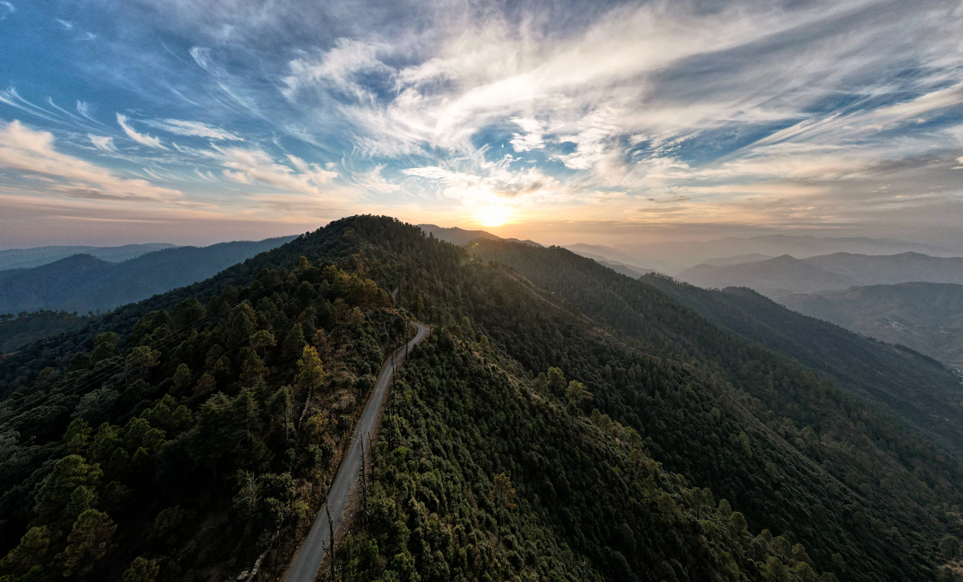 the sun is setting over a mountain with a road going through it